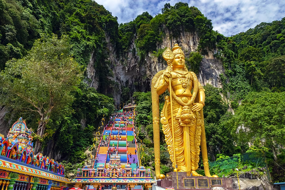 Golden statue with colorful steps leading to a cave, surrounded by lush greenery. People are climbing the stairs under a blue sky.