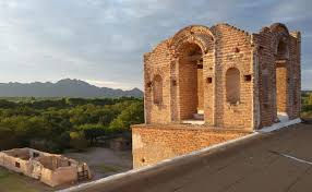 Ancient brick ruins on a rooftop with mountains and trees in the background under a cloudy sky, evoking a historic, serene mood.