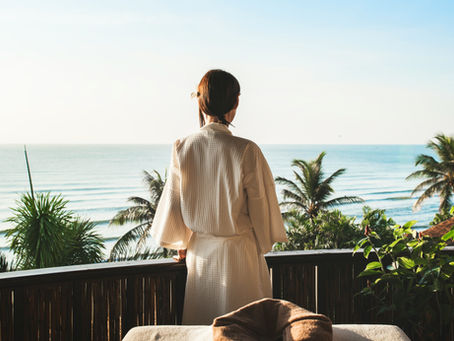 Woman standing on a balcony overlooking the ocean, reflecting on a meaningful travel experience