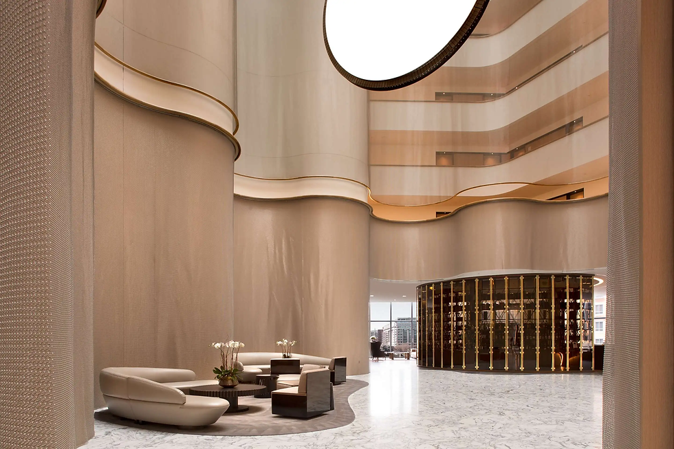 Modern lobby with curved beige walls, marble floor, and circular seating area. Large windows and warm lighting create a welcoming atmosphere.