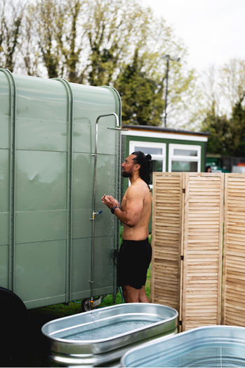 Guest using the outdoor shower beside Revivo Sauna's handcrafted wood-fired outdoor sauna before a cold plunge.
