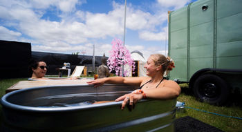 Two guests relaxing in outdoor cold plunge tubs beside Revivo Sauna's wood-fired sauna at a wellness event in Cambridgeshire.