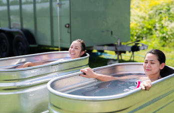 Two guests relaxing in outdoor cold plunge tubs beside Revivo Sauna's wood-fired sauna at Cambridge Rugby Club.