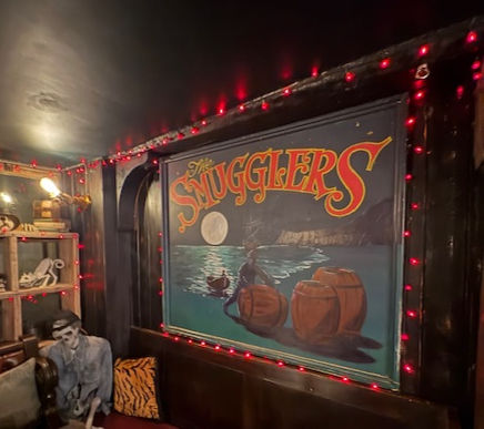 The smugglers Inn in Robin Hood's Bay with "The Smugglers" painting, showing a boat and barrels under a moonlit sky. Red fairy lights, skeleton decoration, cozy vibe.