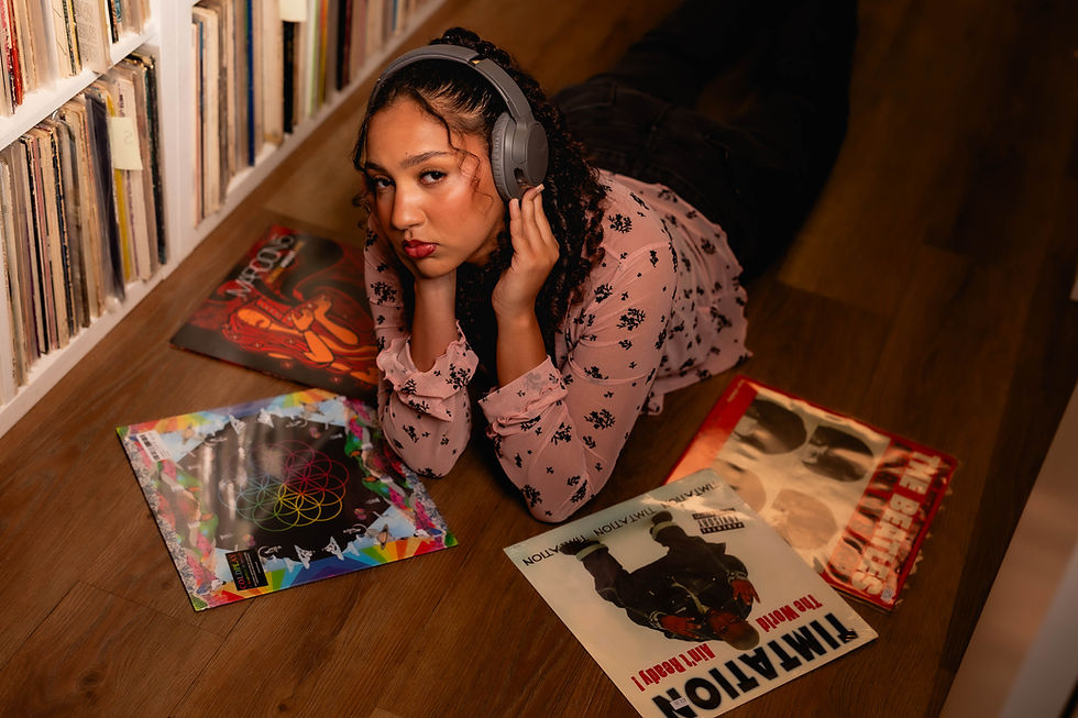 Woman in headphones on a wood floor by record shelves, surrounded by vinyl albums, gazing at the camera in a cozy music room