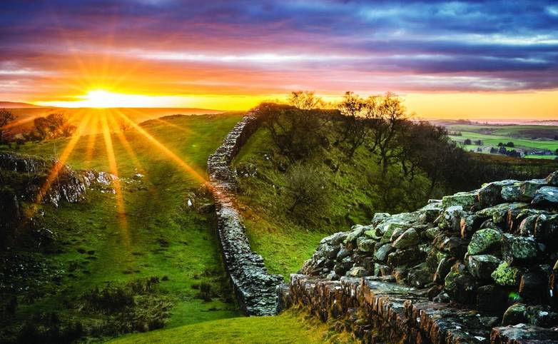 Sunset casts a mystical glow over Hadrian's Wall, illuminating its ancient stones and the lush landscape, evoking a sense of history and wonder.