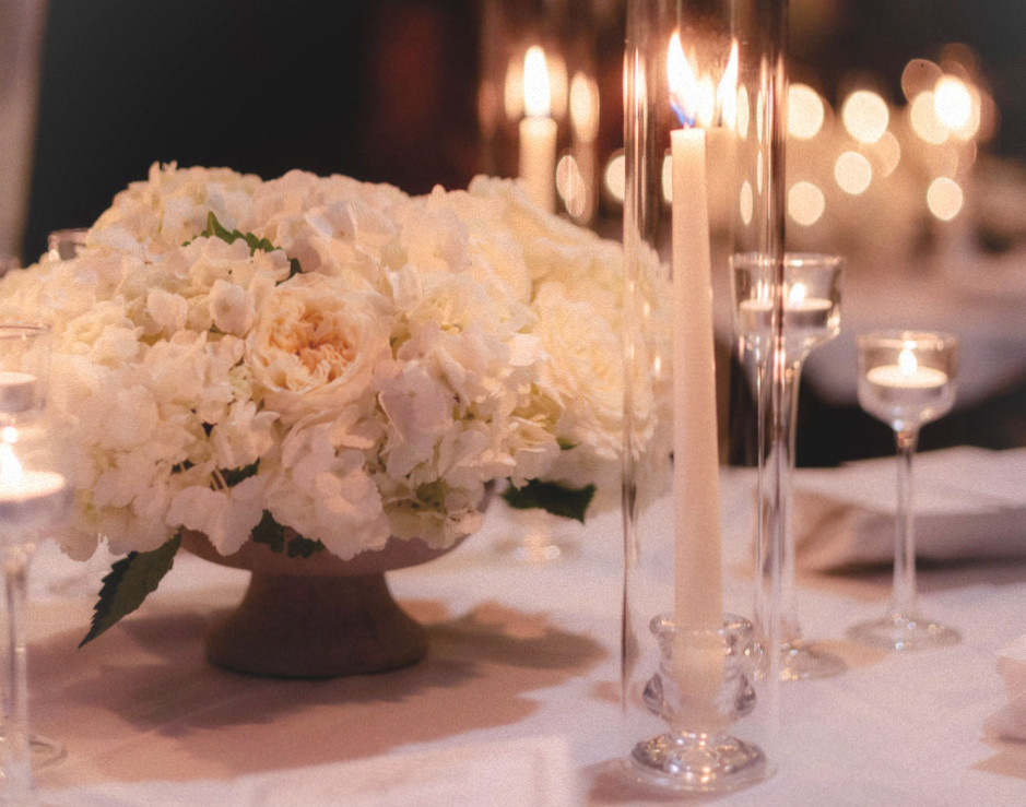Hydrangea centerpiece next to ivory taper candles in hurricane glasses