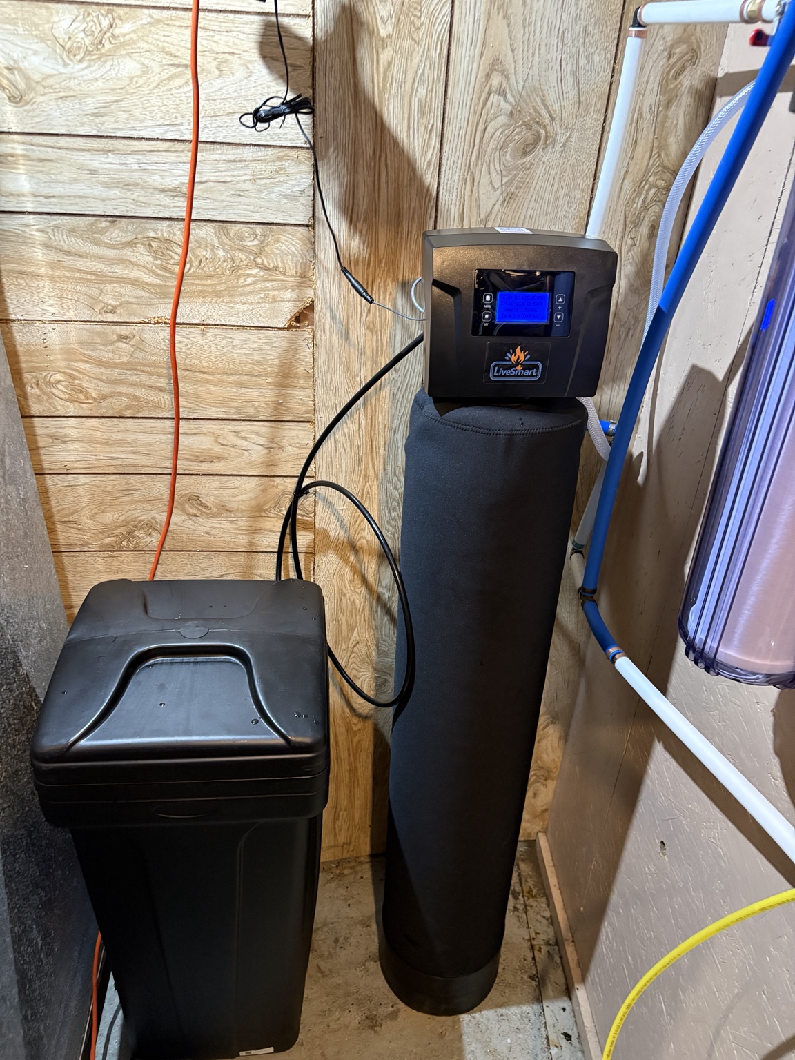 Black LiveSmart softener and separate brine tank in a wood-panelled utility room