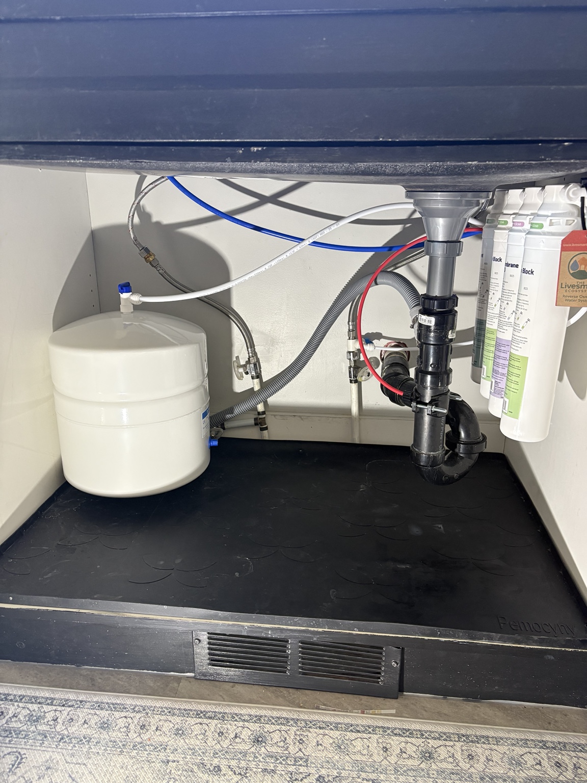 Reverse osmosis cartridges and a white storage tank fitted beneath a kitchen sink in Oliver