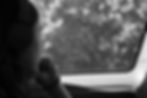 Person with headphones gazes thoughtfully out a car window. Black and white image, blurred trees outside, creating a reflective mood.