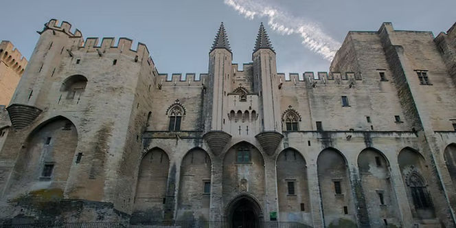 Medieval stone towers, arched entrance, and fortified walls of the Palace of the Popes in Avignon, France.
