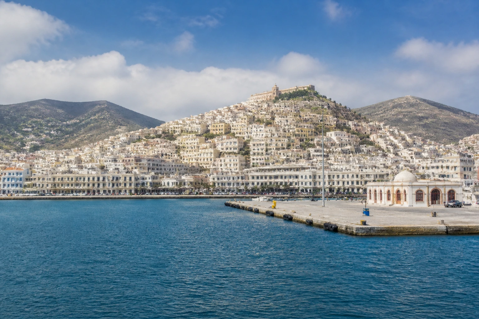 Representative cruise port destination view: Syros, Greece; passenger waterfront and harbor water, not an exact landmark photograph.