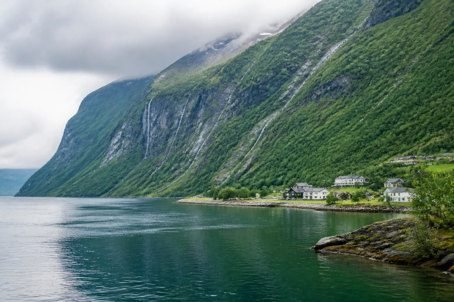 Representative coastal destination view: Geiranger, Norway; coastline and regional vegetation, not an exact landmark photograph.