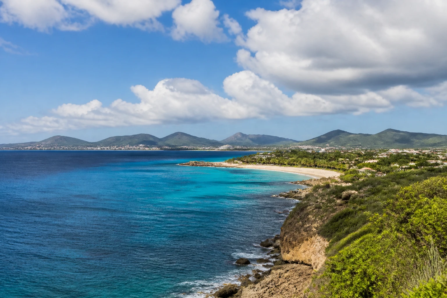 Representative island destination view: Saint Martin and Sint Maarten, France / Netherlands; coastline and regional vegetation, not an exact landmark photograph.