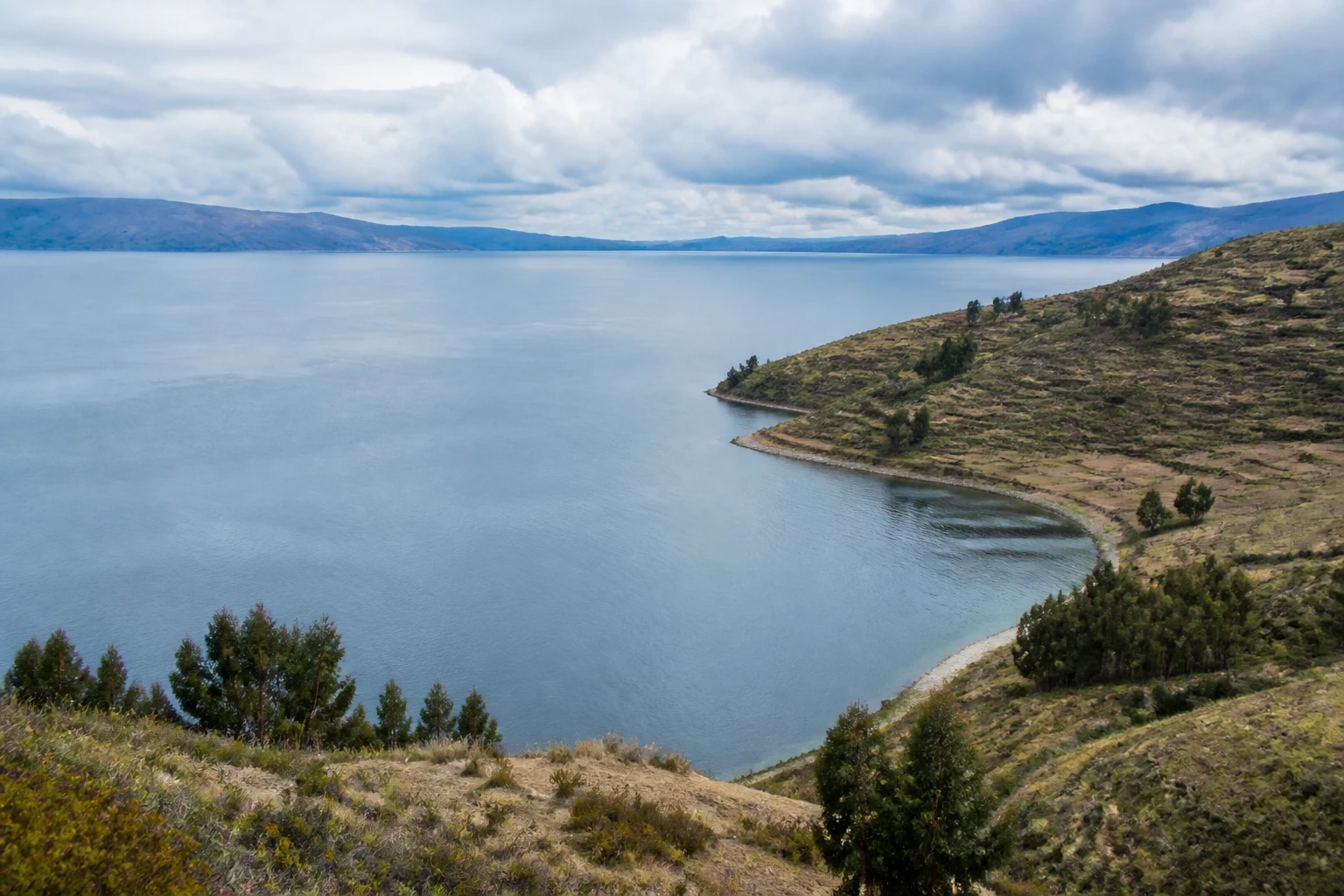 Representative lake destination view: Lake Titicaca, Peru / Bolivia; inland water, regional terrain, and vegetation, not an exact landmark photograph.