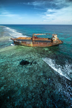 Aerial view of a shipwreck resting on a coral reef during a Belize helicopter tour.
