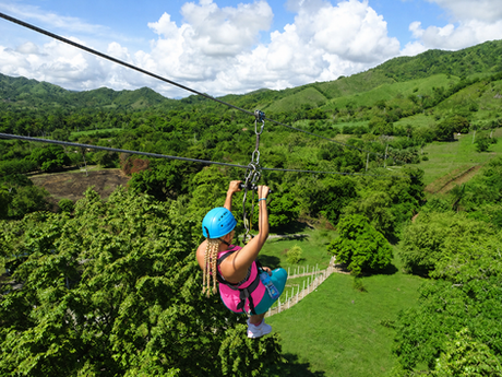 Woman wearing a blue helmet and bright clothing ziplining over tropical mountains near Puerto Plata