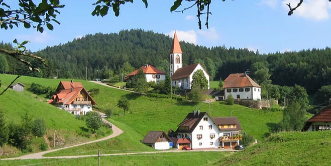 White farmhouses, a church tower and green hills in the Black Forest near Breisach, Germany.