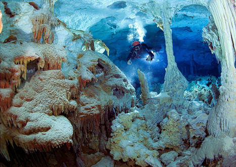 Scuba diver exploring an underwater cave filled with pale rock formations and blue water.