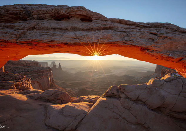 Sunrise starburst beneath Mesa Arch overlooking the canyon landscape in Utah.