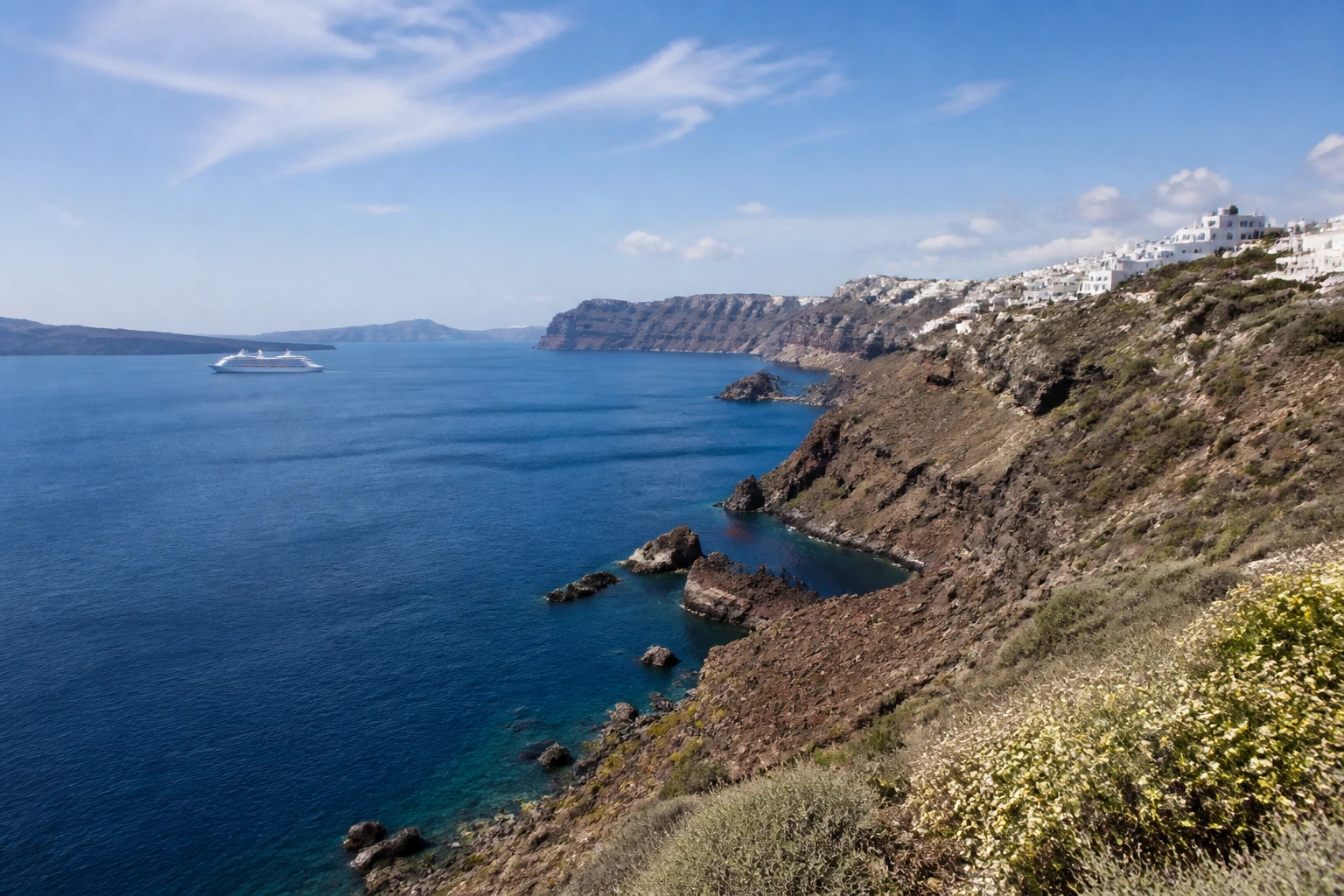 Representative island destination view: Santorini, Greece; coastline and regional vegetation, not an exact landmark photograph.