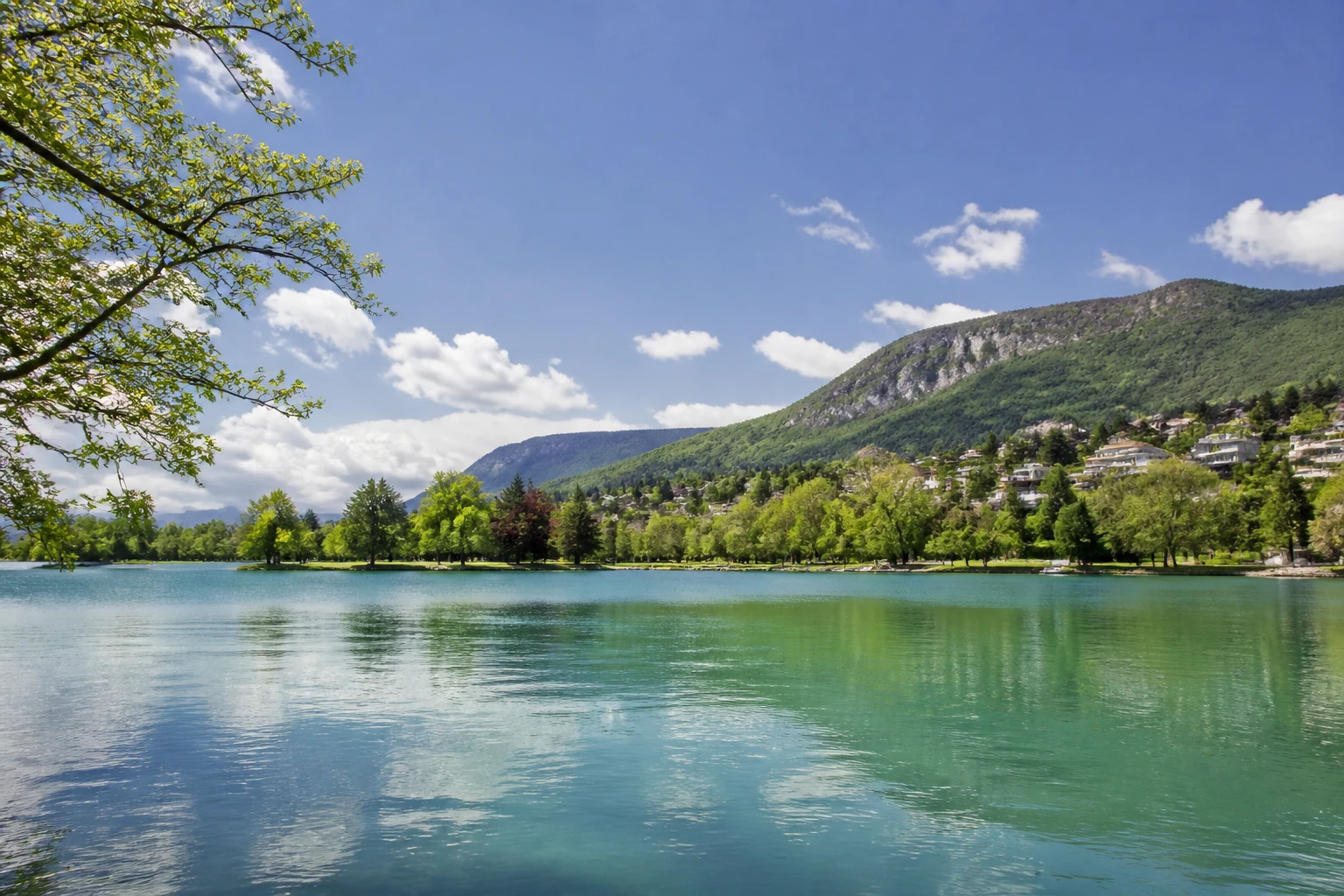 Representative lake destination view of Annecy in France, with inland water, regional terrain, vegetation, and natural light; not an exact landmark photograph.