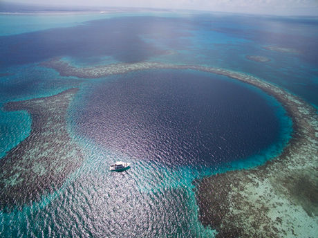 Aerial view of the Great Blue Hole, surrounding coral reef and tour boat in Belize.