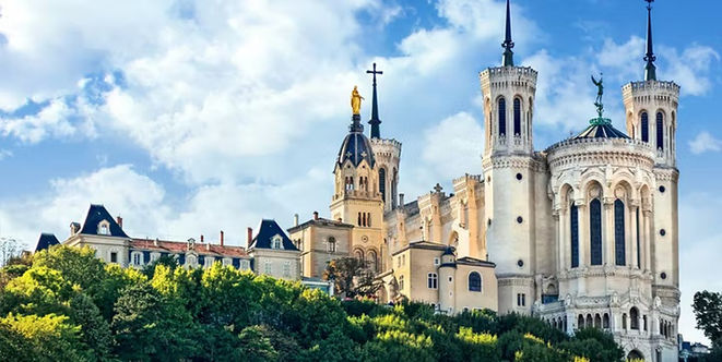 The towers of the Basilica of Notre-Dame de Fourviere rising above a green hillside in Lyon, France.