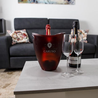 Salotto ampio con bicchieri e prosecco, secchiello personalizzato sul tavolino, ambiente di relax