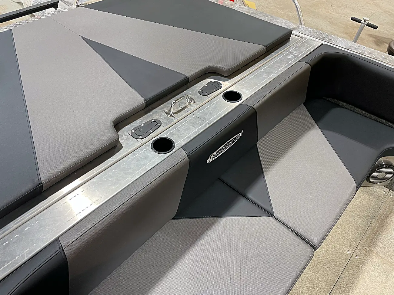 Gray and black boat seats with geometric patterns. Metal trim features cup holders and a handle. In a showroom with a smooth floor.