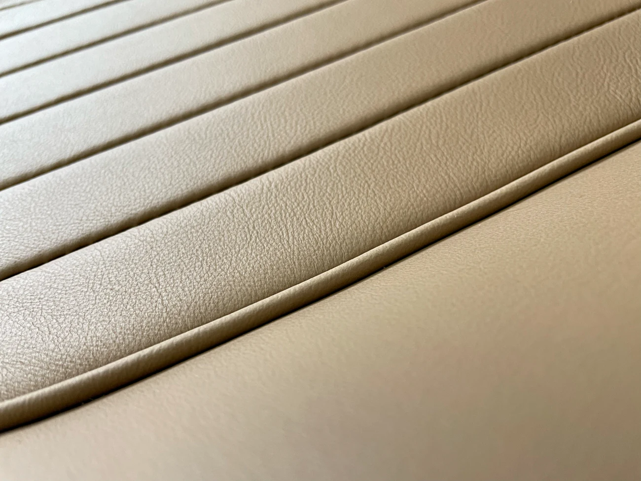 Close-up of beige leather upholstery with parallel seams, showing texture and stitching details.
