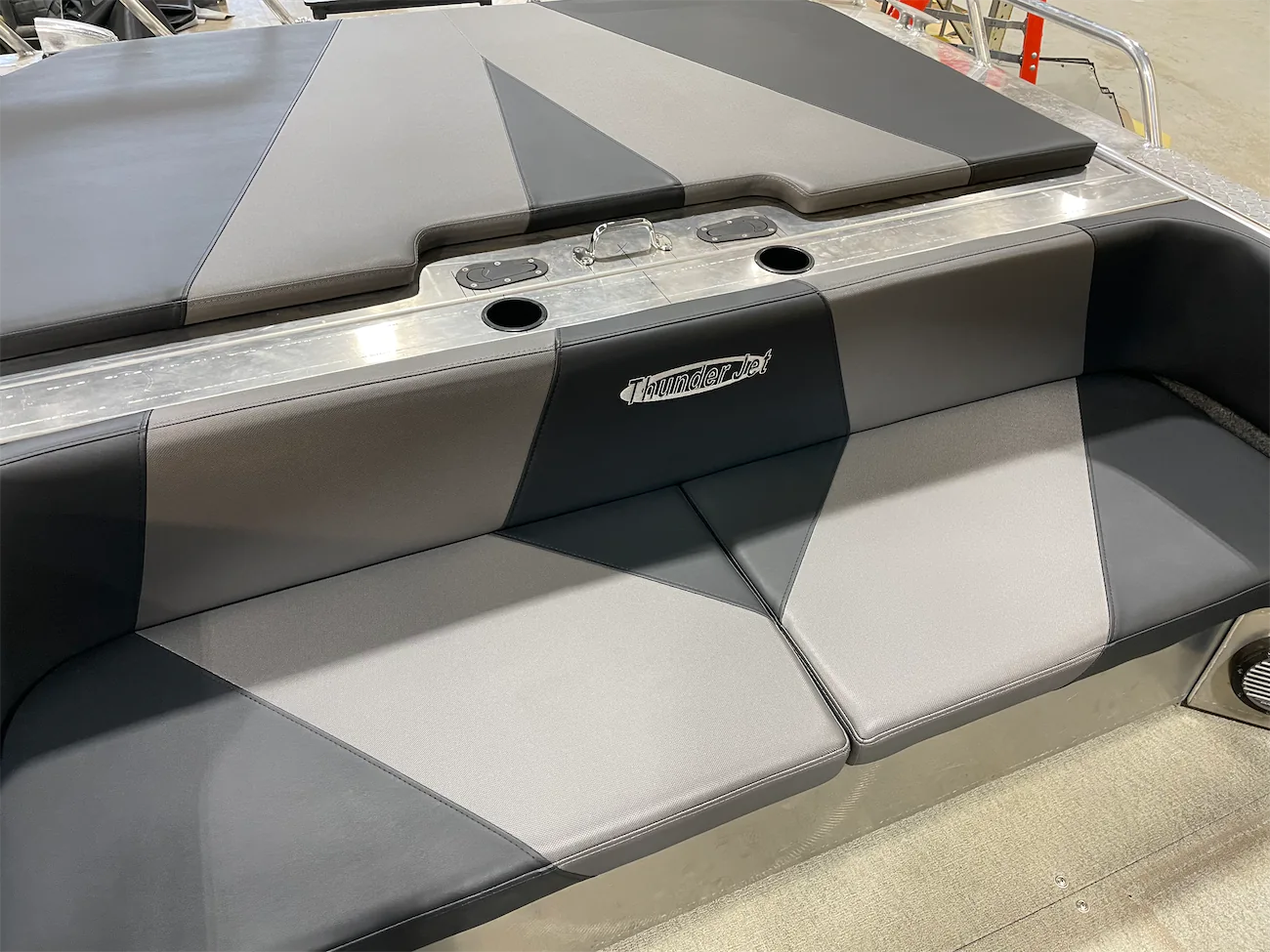 Gray and black boat seat with "Thunder Jet" text. Features cup holders and metallic finish. Indoor setting with industrial background.