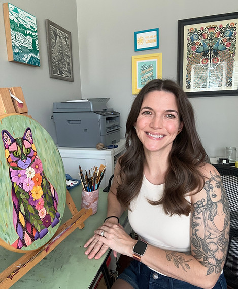 artist Jessica Lancaster sits at her desk next to a cat painting comprised of flowers and leaves