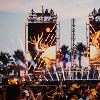 Vue de la scène Sunset avec éclairage orange et public en bord de mer lors du festival de musique électronique
