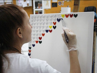lady using a pallet knife to make hearts on an oil painting