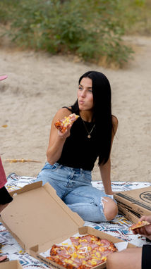 a woman sitting on the beach eating a slice of pizza