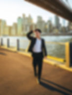 Well-dressed man walking confidently by the waterfront with a city skyline in the background