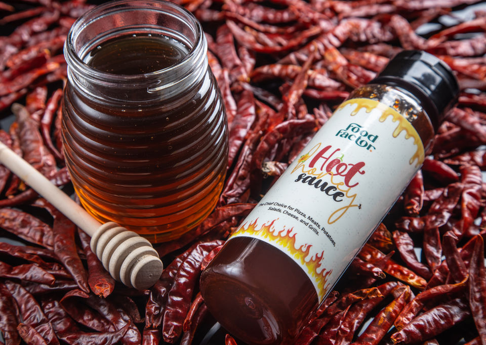 Hot honey bottle surrounded by dried red chili peppers, styled for spicy gourmet product photography in UAE