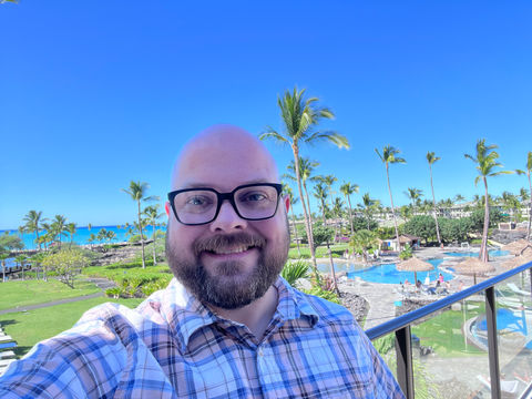 Man on a balcony overlooking palm trees, pools, and the ocean at Waikoloa Beach Marriott Resort on the Island of Hawaii