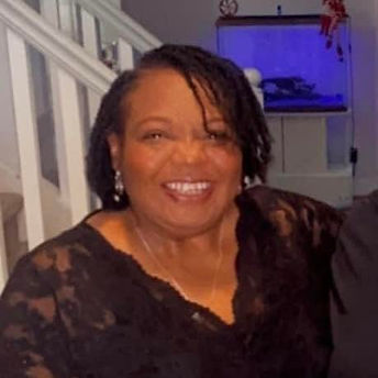 Barbara Bell Tootle headshot of black woman with shoulder length braids in vneck black lace top sitting in fron of white stair rails