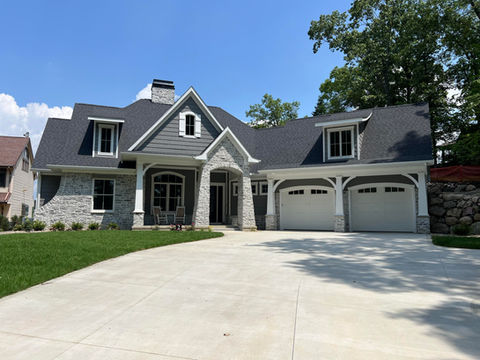 Modern craftsman house design with gray stone and siding, and a shingle roof.
