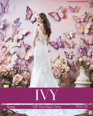 Bride wearing the Ivy wedding gown, a romantic Chantilly lace bridal dress with a fitted sheath silhouette, illusion neckline, delicate lace cap sleeves, and illusion lace back detail. The gown is photographed in front of a soft pink floral and butterfly backdrop at Velvet Bridal. Available off the rack in size 20.