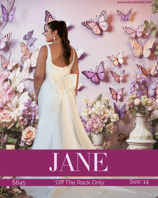Size 14 off-the-rack Jane wedding dress at Velvet Bridal featuring a structured luxury Mikado fabric, square neckline, fitted silhouette, covered buttons down the full train, and optional oversized bow detail on the back, photographed against a floral and butterfly backdrop.