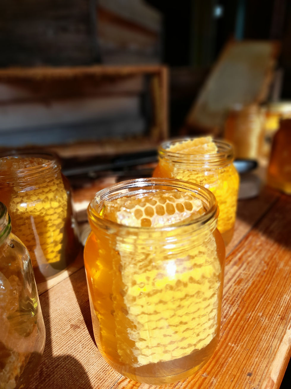 honeycomb in a jar of runny honey on a table with surrounding jars of honey and honeycomb