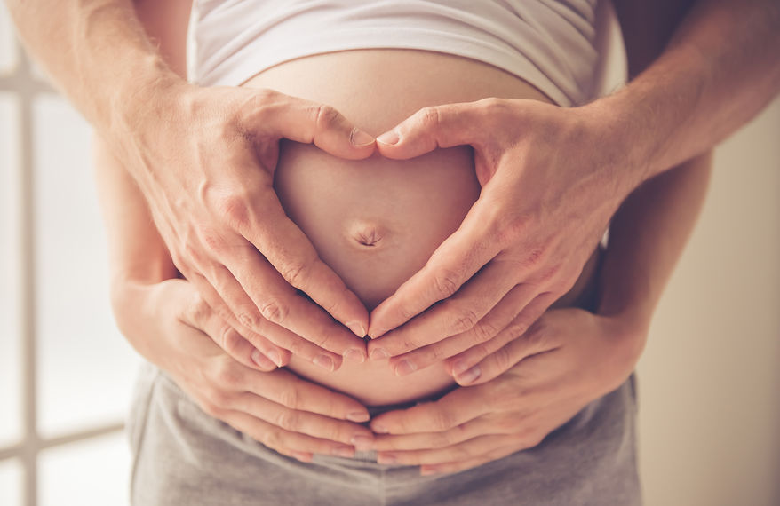 A couple's hands forming a heart shape over a pregnant woman's belly