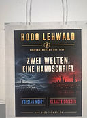 "Papiertüte mit Bodo Lehwald Merchandise-Design: 'Zwei Welten. Eine Handschrift.' – Frisian Noir® und Elbakte Dresden"