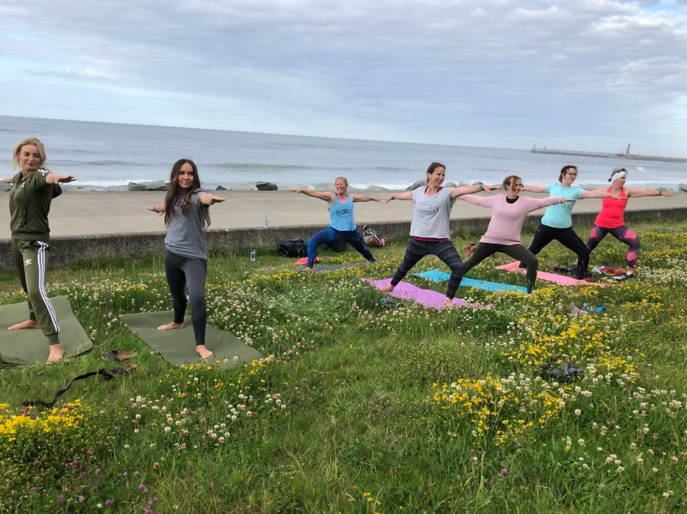 outdoor yoga class performing warrior 2 pose on the grass by the seaside in Whitby.