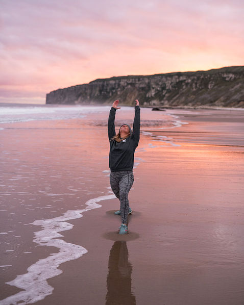 Lady doing Warrior 1 yoga pose on Reighton sands at sunrise
