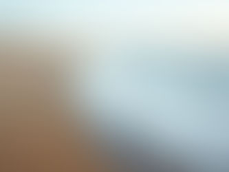 Gentle waves wash onto an empty sandy beach at sunrise, with distant dunes and a calm pastel sky.