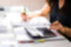 Personne utilisant une calculatrice et prenant des notes sur un bureau, illustrant des activités liées à la comptabilité ou à la gestion financière.